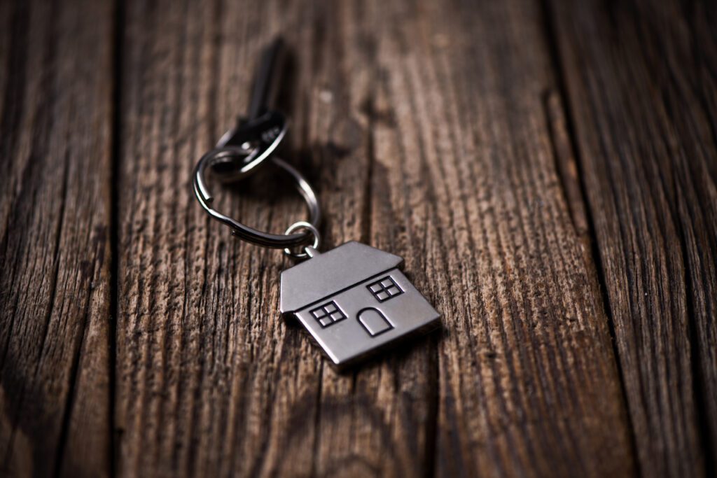 A closeup of key with a house keychain resting on a wood table.