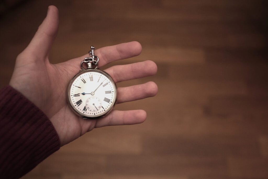 A close up image of a persons hand with a pocket watch as they track how much time their commission management process takes. 