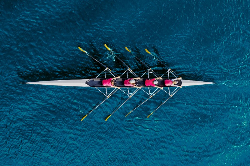 Image shows 4 people in a canoe rowing in tandem representing the synchronicity of loading all of your commission data into one software