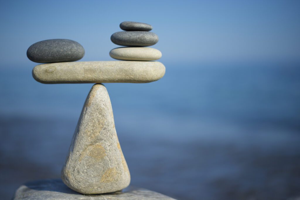 Picture of rocks stacked on top of each other in a pyramid formation balanced on a tiny tip at the top of one larger rock representing the balancing act of managing both payroll and commissions.