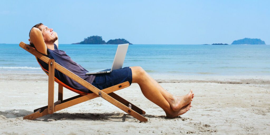 Image of a man reclined in a lounge chair on the beach with a laptop on his lap smiling with his arms crossed behind his head because his commission management process has been simplified.